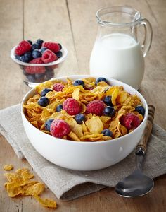 a bowl of cereal with berries and blueberries next to a glass of milk on a wooden table