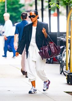 a woman is walking down the street carrying a handbag in her right hand and wearing white pants