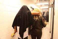 two women walking down a hallway with one carrying a purse and the other covering her face