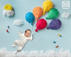 a baby laying in the clouds with balloons