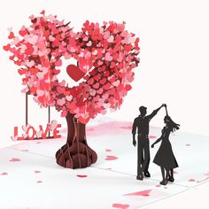 a paper cut out of a man and woman next to a tree with hearts