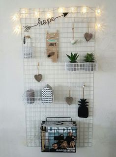 a white wire wall hanging on the side of a wall filled with plants and other items