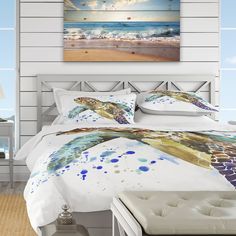 a bed with white sheets and blue watercolor paint on it, along with an ocean view