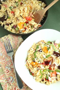 two bowls filled with pasta and vegetables on top of a green table cloth next to a wooden spoon