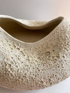 a white vase sitting on top of a table next to a wall with holes in it