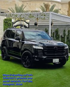 a black suv parked on top of a lush green field next to a white fence