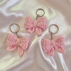 three pink crocheted bow keychains laying on a white satin surface,