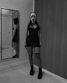 a woman wearing a mask standing in front of a mirror with her hands on her hips