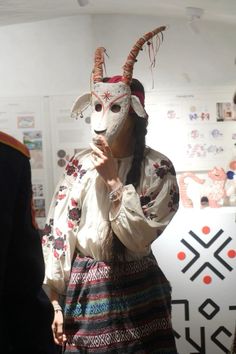 a woman wearing a goat mask standing in front of a wall