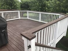 a deck with white railings and an outdoor grill cover on the top, surrounded by trees