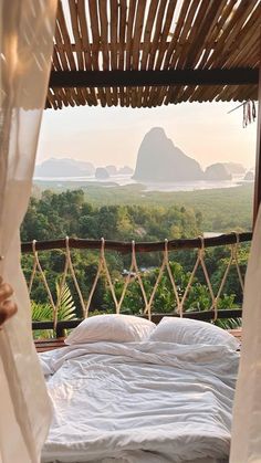 a bed sitting under a canopy next to a lush green forest covered hillside with mountains in the distance