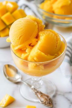 two bowls filled with yellow ice cream next to silver spoons on a white table