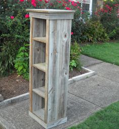 a tall wooden cabinet sitting on top of a sidewalk next to a flower bed and bushes