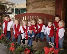 a group of children wearing red scarves sitting on a wooden bench in front of a christmas tree