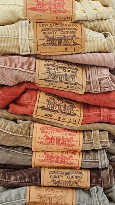 many different colored shirts are stacked on top of each other, with labels reading quality clothing