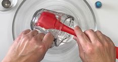 two hands are using a red blender to mix liquid in a glass bowl on top of a stove