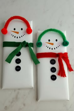 two snowmen made out of white paper with green and red hair