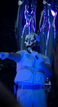 a man dressed in white standing next to two large metal sculptures with blue lights on them