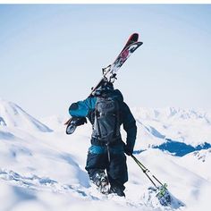 a man walking up the side of a snow covered slope with skis on his back