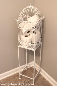 a white birdcage filled with toilet paper on top of a floor next to a wall