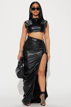 a woman wearing a black leather skirt and crop top with high slits, standing in front of a white background