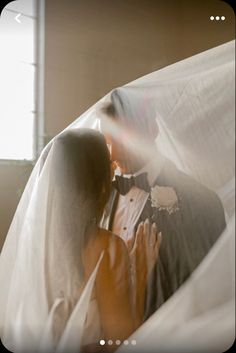 a man and woman are kissing under the covers of their wedding veils in front of a window