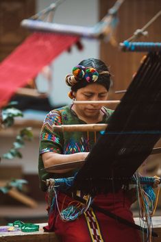 a woman is weaving fabric on a loom with an instrument in her hand and she is looking down at the yarn