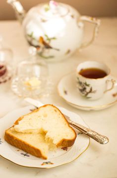 a piece of bread on a plate next to a cup of tea and a teapot