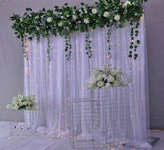 two white vases with flowers and greenery hanging from the ceiling