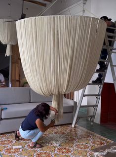 a woman is working on a couch in a room with white drapes hanging from the ceiling