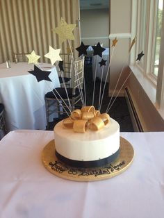 a white cake with gold bow and stars on top sitting on a table in front of a window