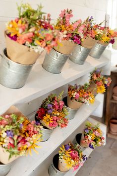 several metal buckets filled with colorful flowers on top of a white shelf in a room