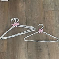 a pair of white pearls hangers with pink bows on them, sitting on a wooden floor