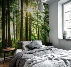 a bed sitting under a window next to a forest wall mural