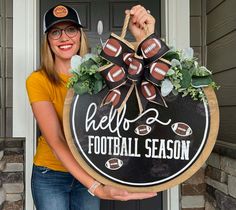 a woman holding up a football sign in front of a door that says hello football season