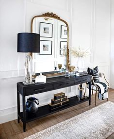 a black console table with a mirror, lamp and pictures on the wall behind it