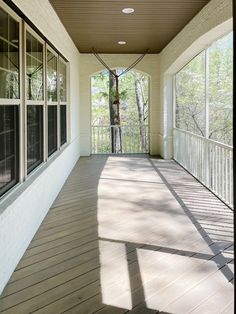 an empty porch with sun shining through the windows and trees in the backgroud