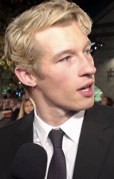 a close up of a person in a suit and tie talking to someone with a microphone