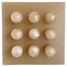 six white balls are placed in a square shape on a beige background, with one smaller ball at the center