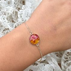 a woman's arm wearing a bracelet with an orange and pink glass bead