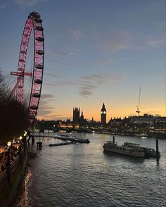 the ferris wheel is lit up at night in front of the river thames and big ben