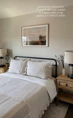 a bed with white linens and pillows in a bedroom next to a painting on the wall