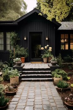 a black house with potted plants and steps leading to the front door is shown