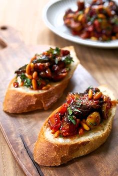 two pieces of bread with meat and vegetables on them sitting on a wooden cutting board