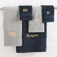 three towels hanging on a towel rack next to a white brick wall with gold lettering