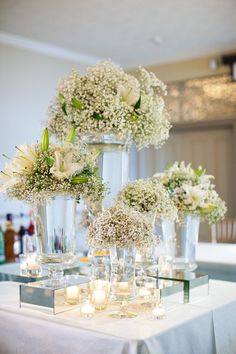 three tall vases filled with white flowers on top of a table covered in candles