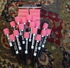 pink and black marker pens sitting on top of a carpet next to a box of erasers