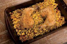 a pan filled with chicken and corn on top of a wooden table