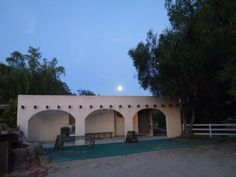 an old adobe building is lit up at night with the moon in the sky behind it