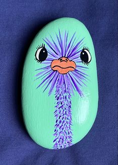 a painted rock with an ostrich's face and purple flowers on it